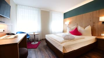 Habitación de hotel con cama, escritorio, silla, televisión y ventana con cortinas.