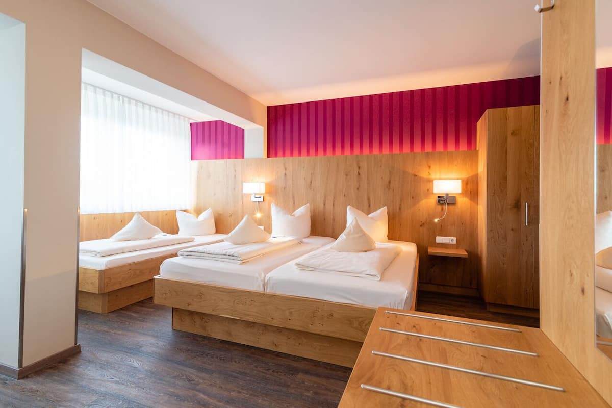 A hotel room with two beds, a wooden wardrobe, and a small seating area.