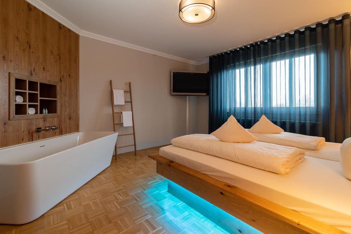 A modern bedroom with a large bathtub, a flat-screen TV, and a window with curtains.