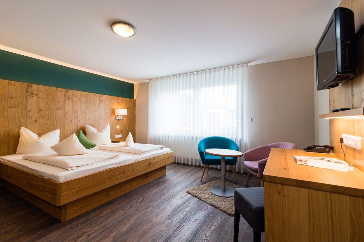 A hotel room with a wooden bed, a desk, a chair, a television, and a window with curtains.