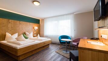 Habitación de hotel con una cama de madera, un escritorio, una silla, un televisor y una ventana con cortinas.