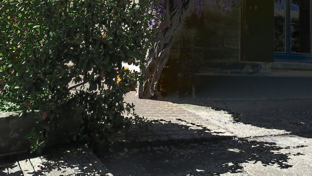 Un edificio con fachada tradicional, pared de piedra y un pequeño jardín con plantas de flores moradas.