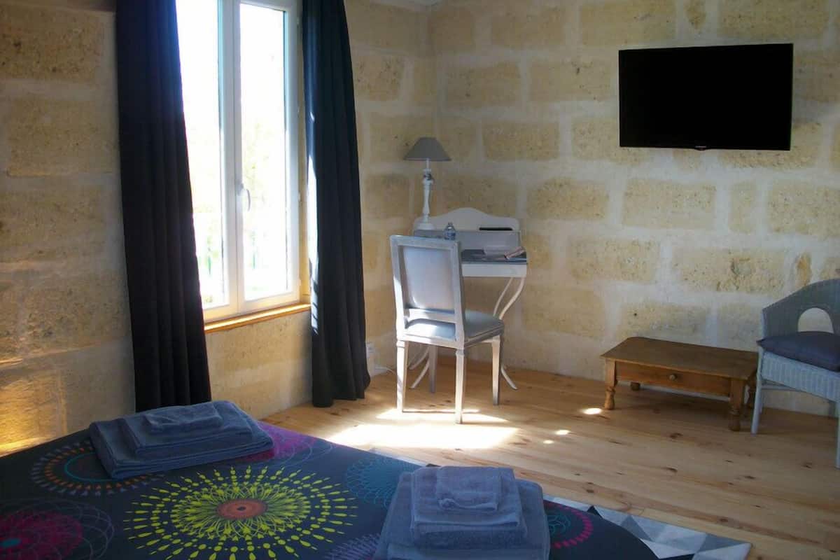 A room with a bed, a desk, a chair, and a television on the wall.