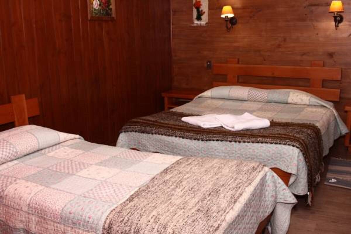 Una habitación con dos camas de madera, cada una con una colcha estampada. Hay lámparas de pared a cada lado de las camas.