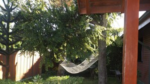 A hammock hanging between two trees in a backyard with a wooden fence and a house in the background. - Hostal el Nogal Pucón (Pucón)