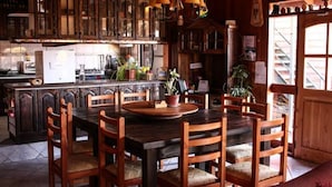 A wooden dining table with chairs, a kitchen area with cabinets and appliances, and a staircase leading to an upper level. - Hostal el Nogal Pucón (Pucón)