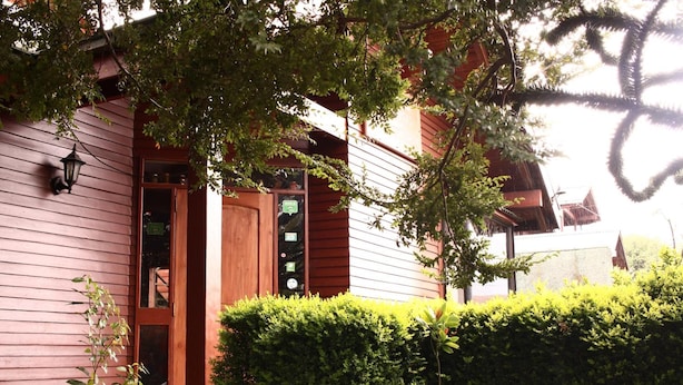 A wooden building with a door and windows, surrounded by greenery. - Hostal el Nogal Pucón (Pucón)