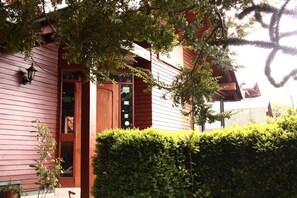 A wooden building with a door and windows, surrounded by greenery. - Hostal el Nogal Pucón (Pucón)