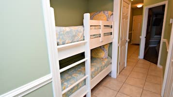 A bunk bed with floral bedding in a hallway with green walls and tiled flooring.