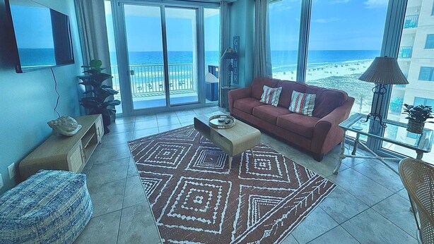 A living room with a red sofa, a patterned rug, a TV, and a view of the beach.