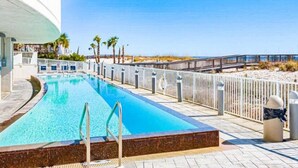 A swimming pool with a wooden deck, a white fence, and palm trees in the background.