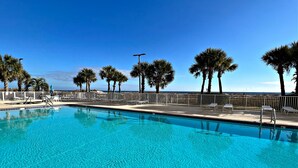 A clear blue pool with a white deck, surrounded by palm trees and a white fence. - What if I told you…You CAN afford Paradise! Make the Call today! 🤙 (Orange Beach)