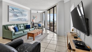 Ein modernes Wohnzimmer mit einem grünen Sofa, einem Holztisch, einem Flachbildfernseher und einem großen Fenster mit Blick.