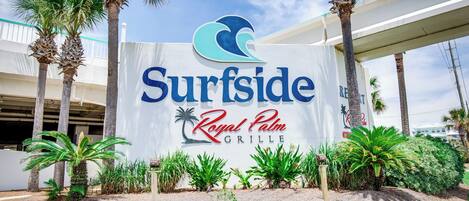 Une enseigne pour le restaurant Surfside Royal Palm Grille, avec des palmiers et un ciel dégagé.