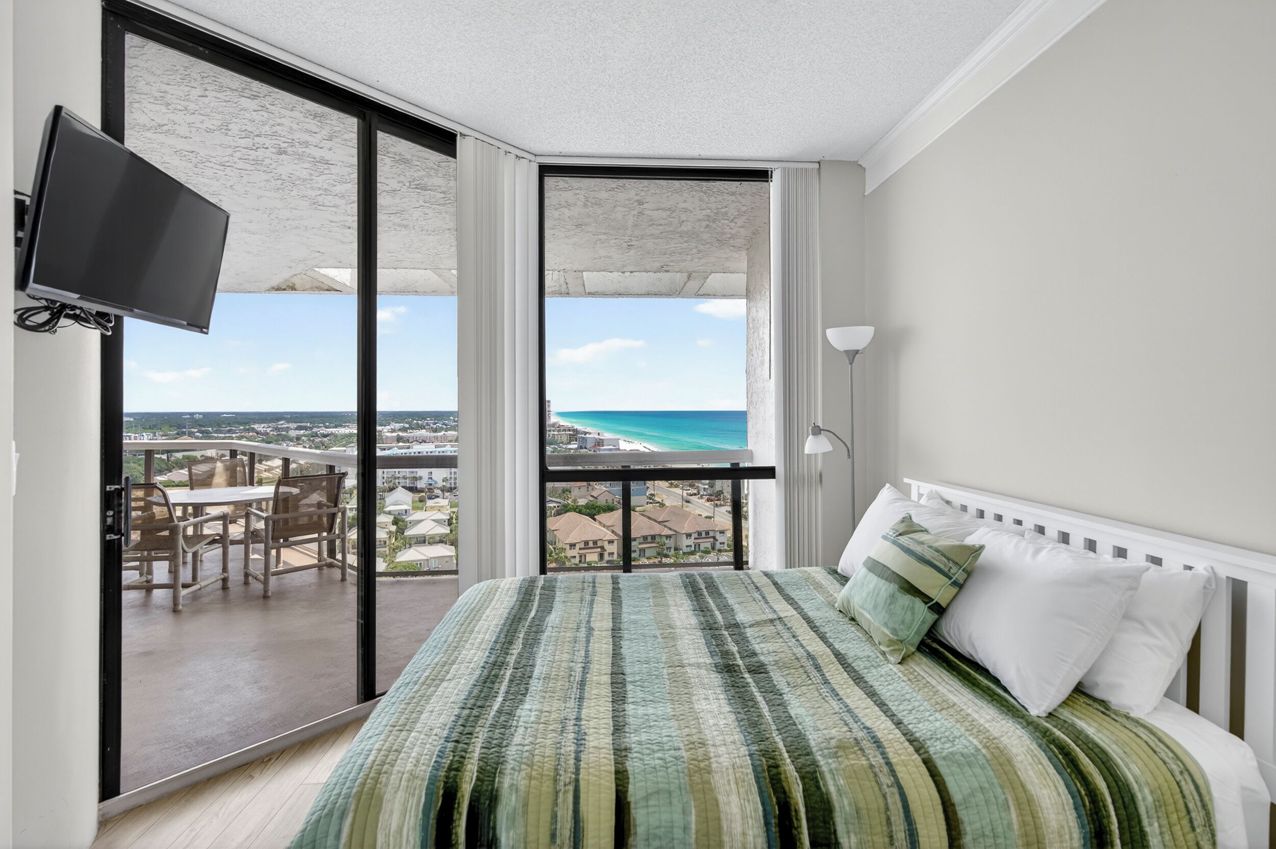 Ein Schlafzimmer mit einem großen Bett, einem an der Wand befestigten Fernseher und einem Balkon mit Blick auf den Strand.