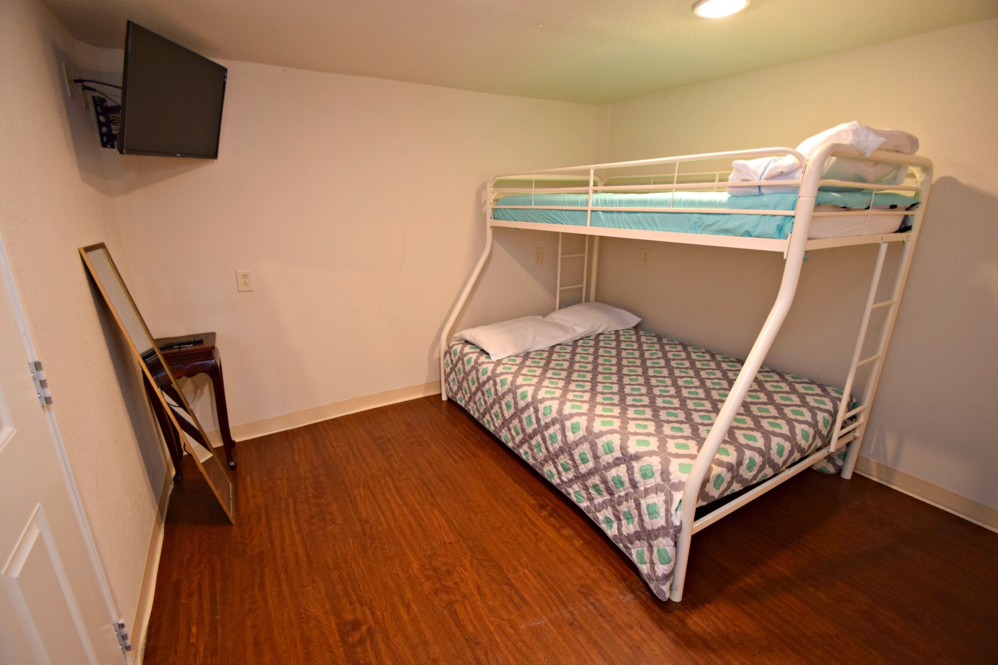 Een stapelbed met beddengoed met dessin, een houten vloer, een aan de muur bevestigde televisie en een kleine houten stoel.