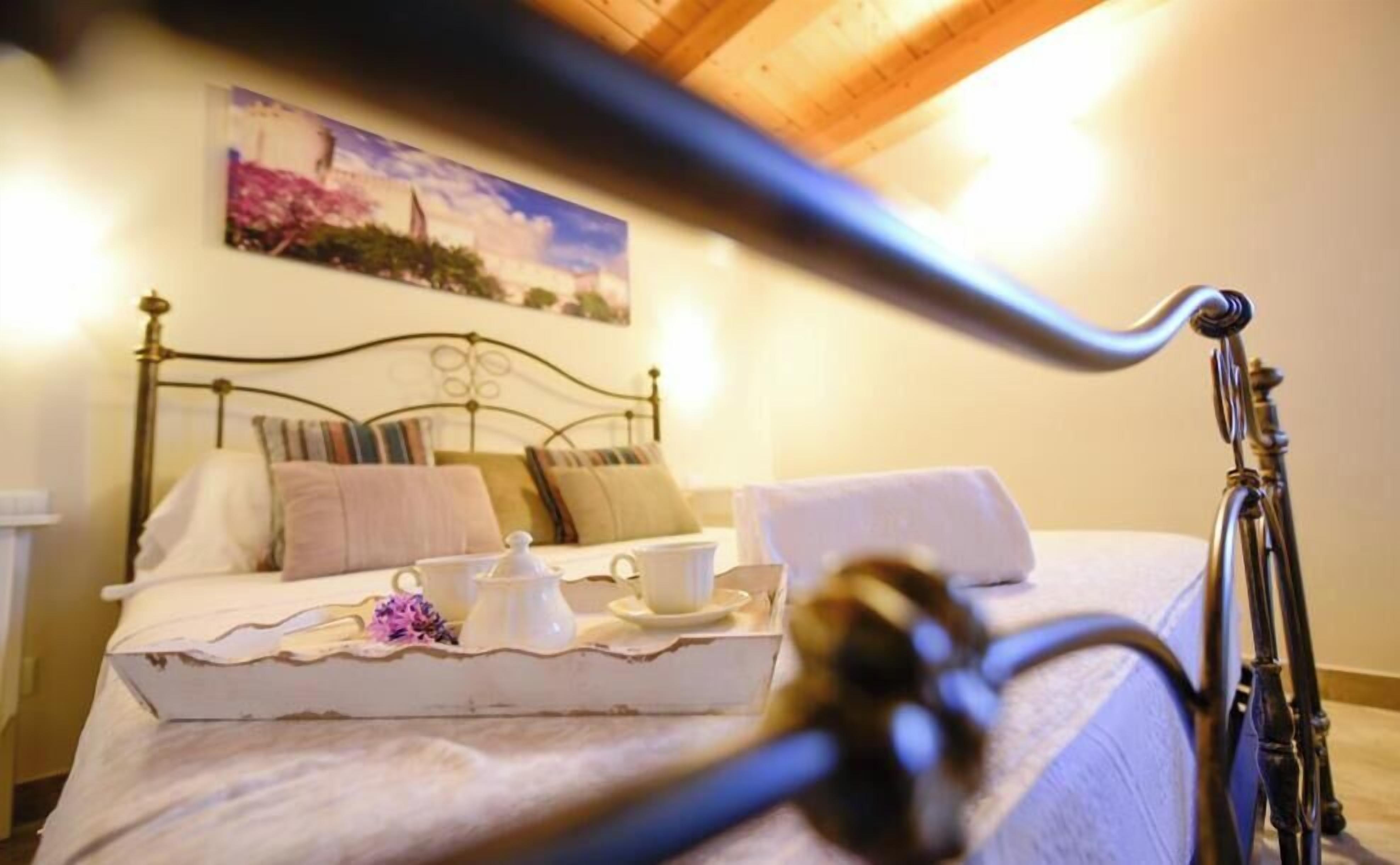 A neatly made bed with a tray of tea items, a painting on the wall, and a wooden ceiling.