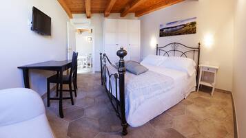 A bedroom with a bed, a desk, and chairs. There is a painting on the wall and a window with a view.