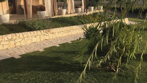 Un espacio al aire libre techado con paredes de piedra, plantas en macetas y un sendero cubierto de césped.