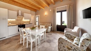 Una cocina moderna con armarios blancos, una mesa de comedor con sillas, un sofá y un televisor montado en la pared.