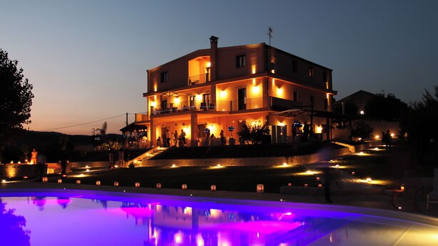 Un edificio de varios pisos con balcones, una piscina con bordes iluminados y un exterior bien iluminado.