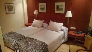 Una cama doble con dos almohadas, una mesita de noche con lámpara, una silla y una pequeña mesa con teléfono.