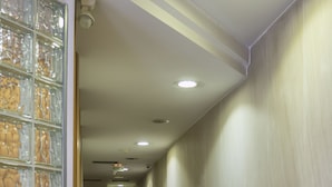 Un pasillo con piso de mármol, pared de bloques de vidrio y una puerta al final.