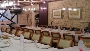 Un salón de banquetes con largas mesas dispuestas para el servicio de comidas, sillas y lámparas colgantes.