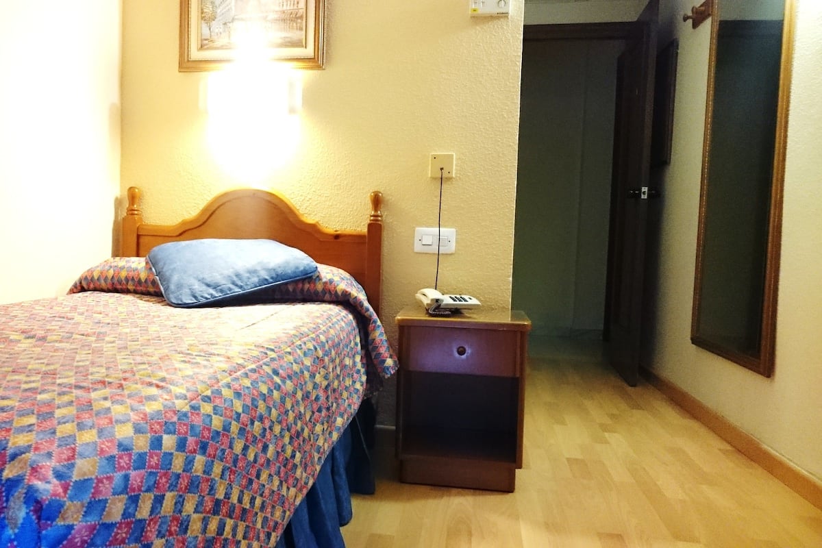 A hotel room with a bed, a bedside table with a phone, and a door.