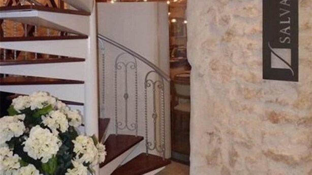 Una escalera con barandillas blancas y peldaños de madera que lleva a una habitación con pared de piedra y un letrero que dice "SALVADORA".