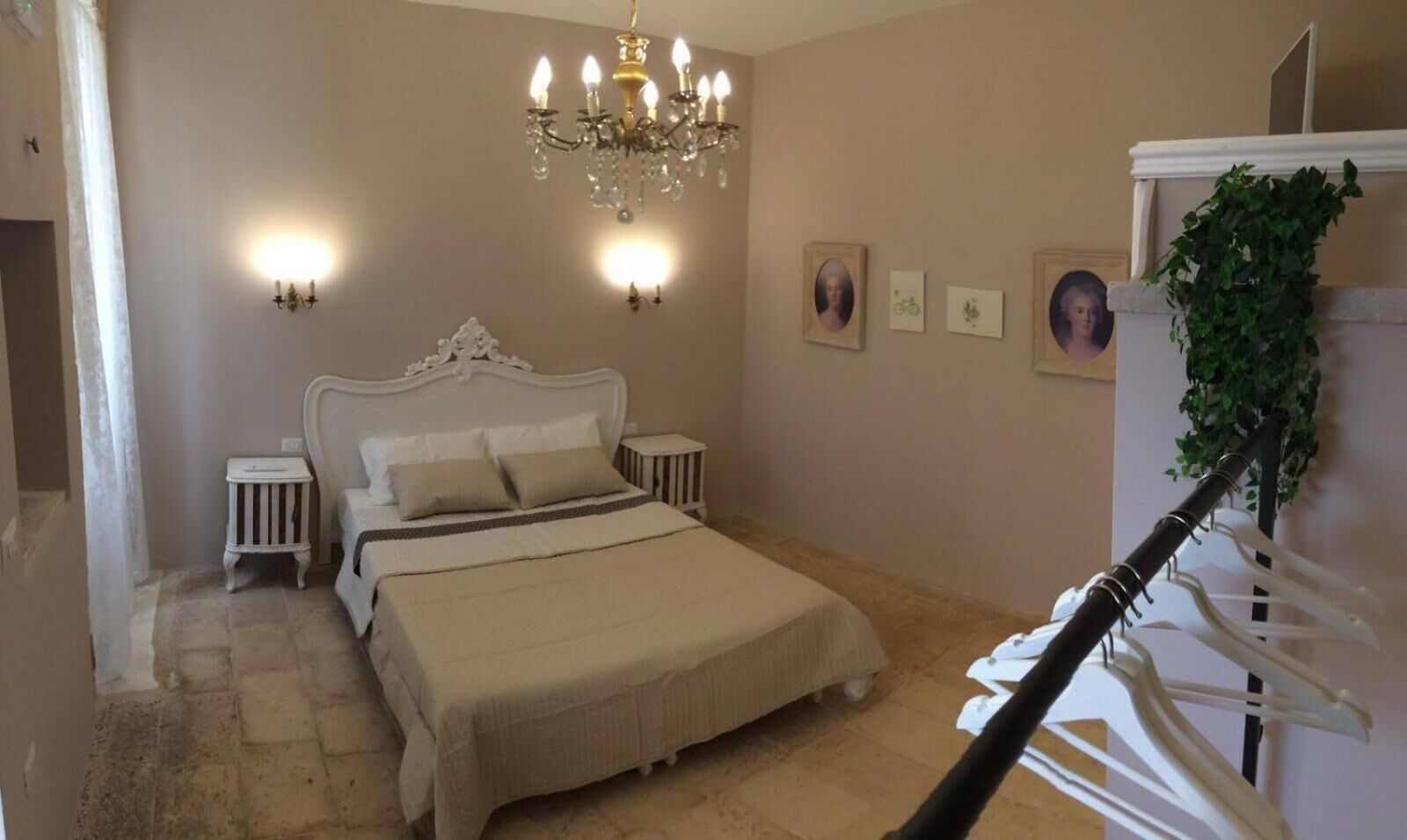 A bedroom with a large bed, a chandelier, bedside tables, and wall-mounted lights.