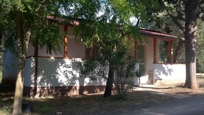A building with a white exterior and a red roof, surrounded by trees and a dirt path.