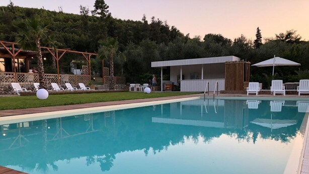 A swimming pool with a wooden deck, lounge chairs, and a covered seating area.