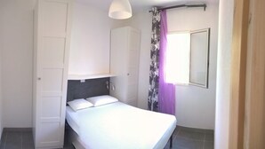 A bedroom with a bed, a wardrobe, a mirror, and a window with curtains.