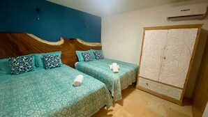 A hotel room with two beds, each with patterned bedding and pillows, a wooden headboard, a wardrobe with a decorative panel, and a ceiling light.