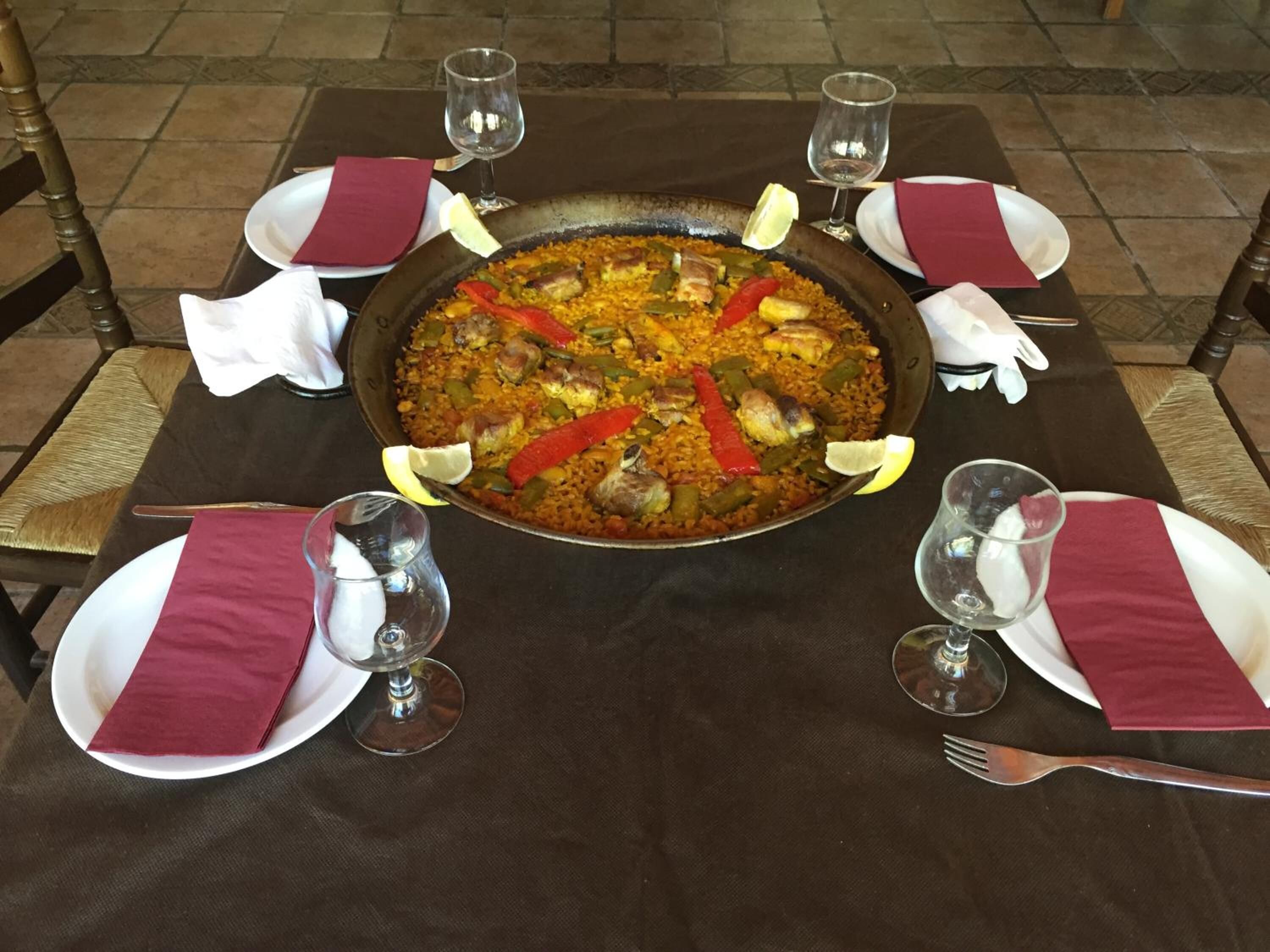 A large, round, shallow pan filled with a rice dish, surrounded by plates, glasses, and cutlery on a table.