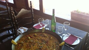 Ett matbord med en stor stekpanna full av paella, en flaska vin och flera glas.