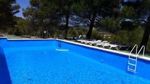 En klarblå pool med en stege, omgiven av solstolar och träd.