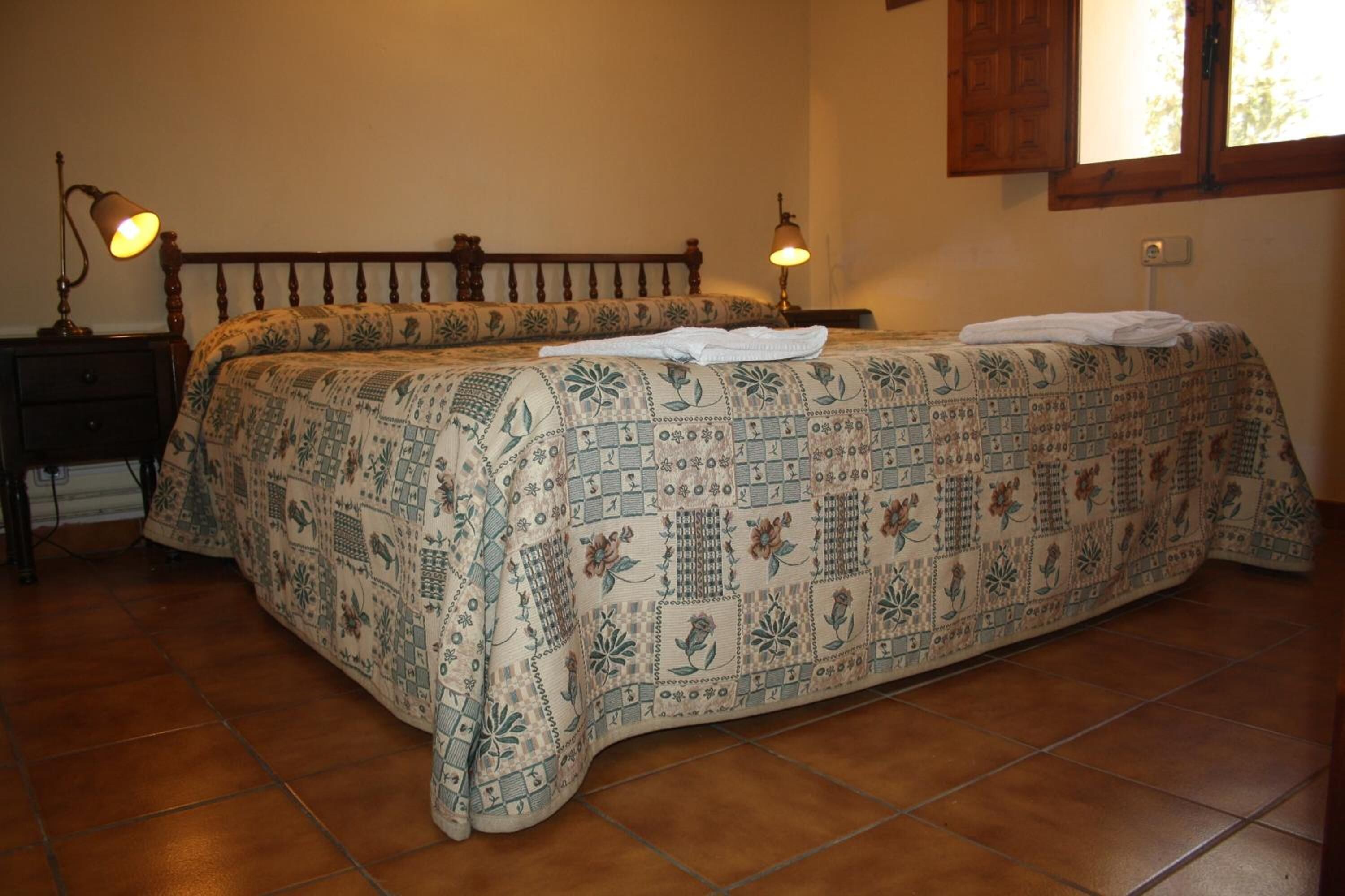 A bed with a patterned bedspread, two bedside lamps, and a wooden headboard.