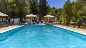 Una piscina rectangular con agua cristalina y azul, rodeada de sillas de descanso y sombrillas.