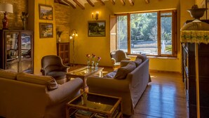 Una sala de estar acogedora con un sofá, sillones, una mesa de centro y una chimenea. Hay cuadros en las paredes y una ventana con vistas a árboles.