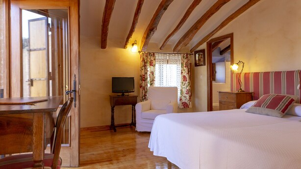 A cozy bedroom with a wooden ceiling, a bed with striped pillows, a bedside table with a lamp, and a television on a small table.