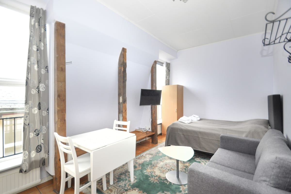Habitación de hotel con cama, sofá, una mesita, televisor y ventana con cortinas.