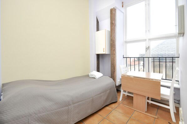 A small, neatly arranged bedroom with a single bed, a wooden desk, and a window with a view of the city. - Boende Visby (Visby)