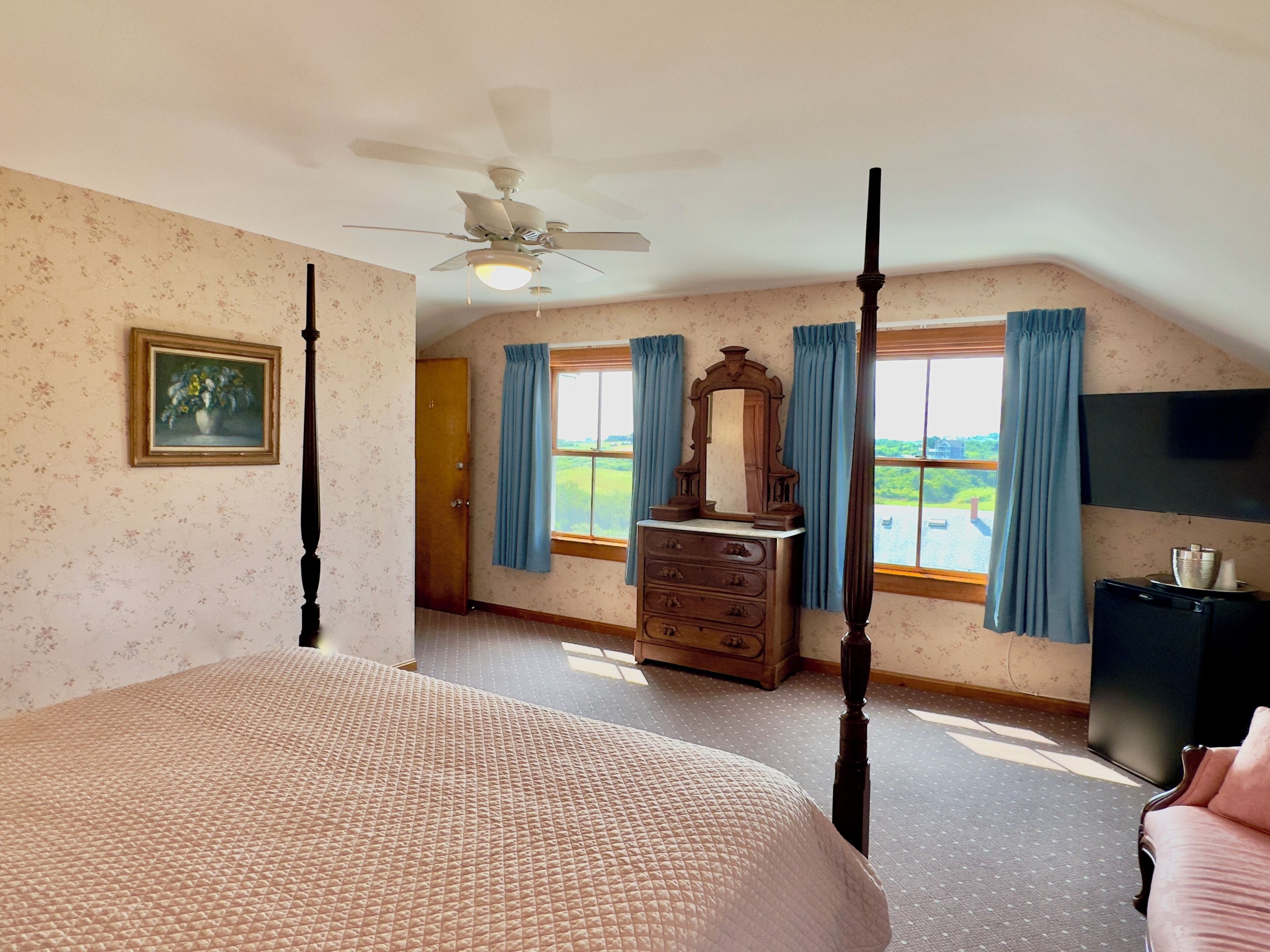 A bedroom with a four-poster bed, a dresser, a vanity with a mirror, and a ceiling fan.