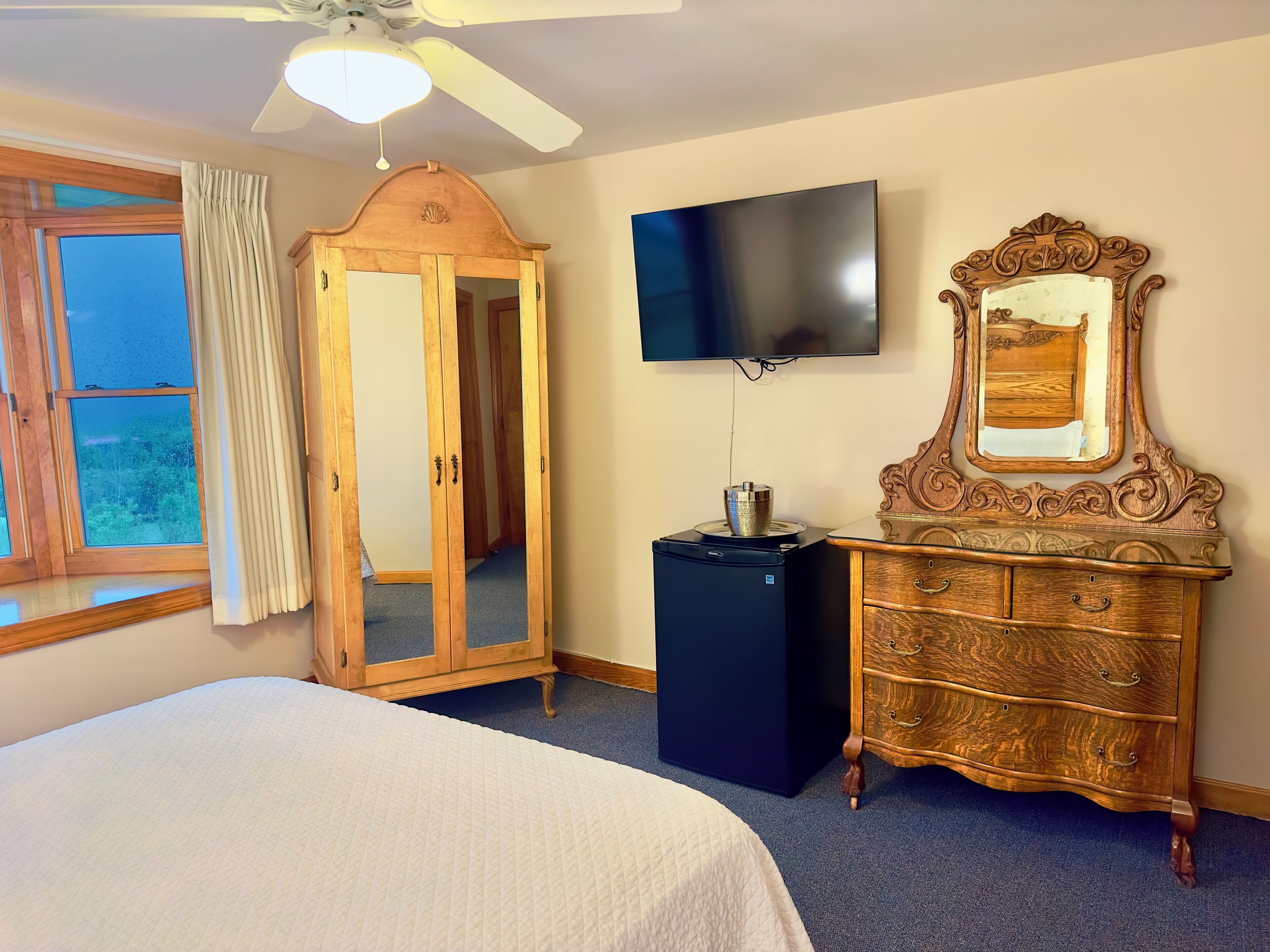A bedroom with a bed, a wardrobe, a television, and a ceiling fan.