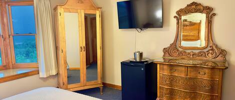 A bedroom with a bed, a wardrobe, a television, and a ceiling fan.