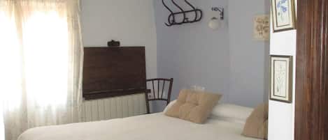 Un dormitorio con una cama grande, una silla, un radiador y ganchos en la pared.