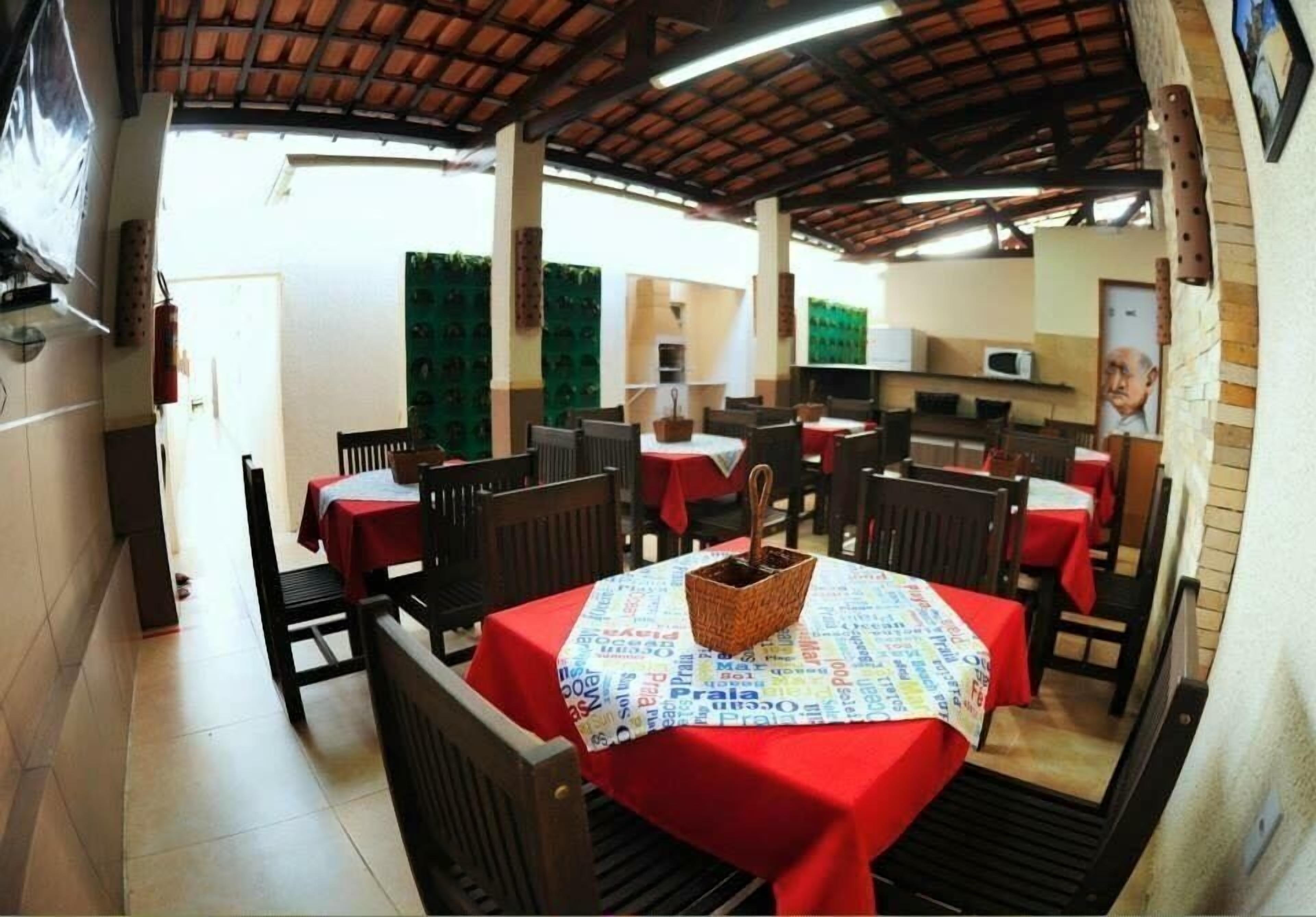 A restaurant with multiple tables covered with red tablecloths, wooden chairs, and a central table with a woven basket.