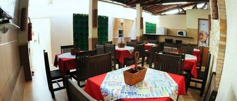 A restaurant with multiple tables covered with red tablecloths, wooden chairs, and a central table with a woven basket.